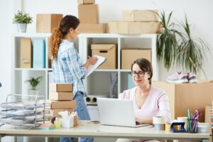 Online shop office manager networking while her colleague making notes